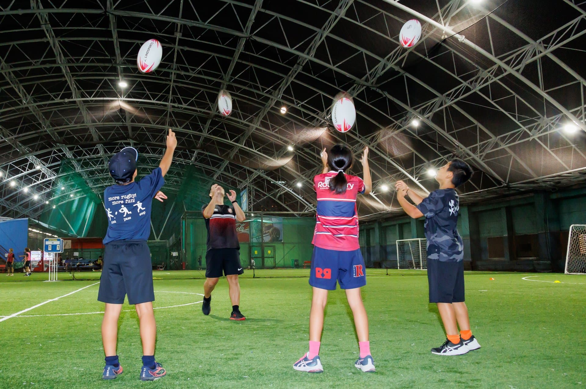 ドーム内でラグビーボールを投げ上げる小・中学生の選手たち