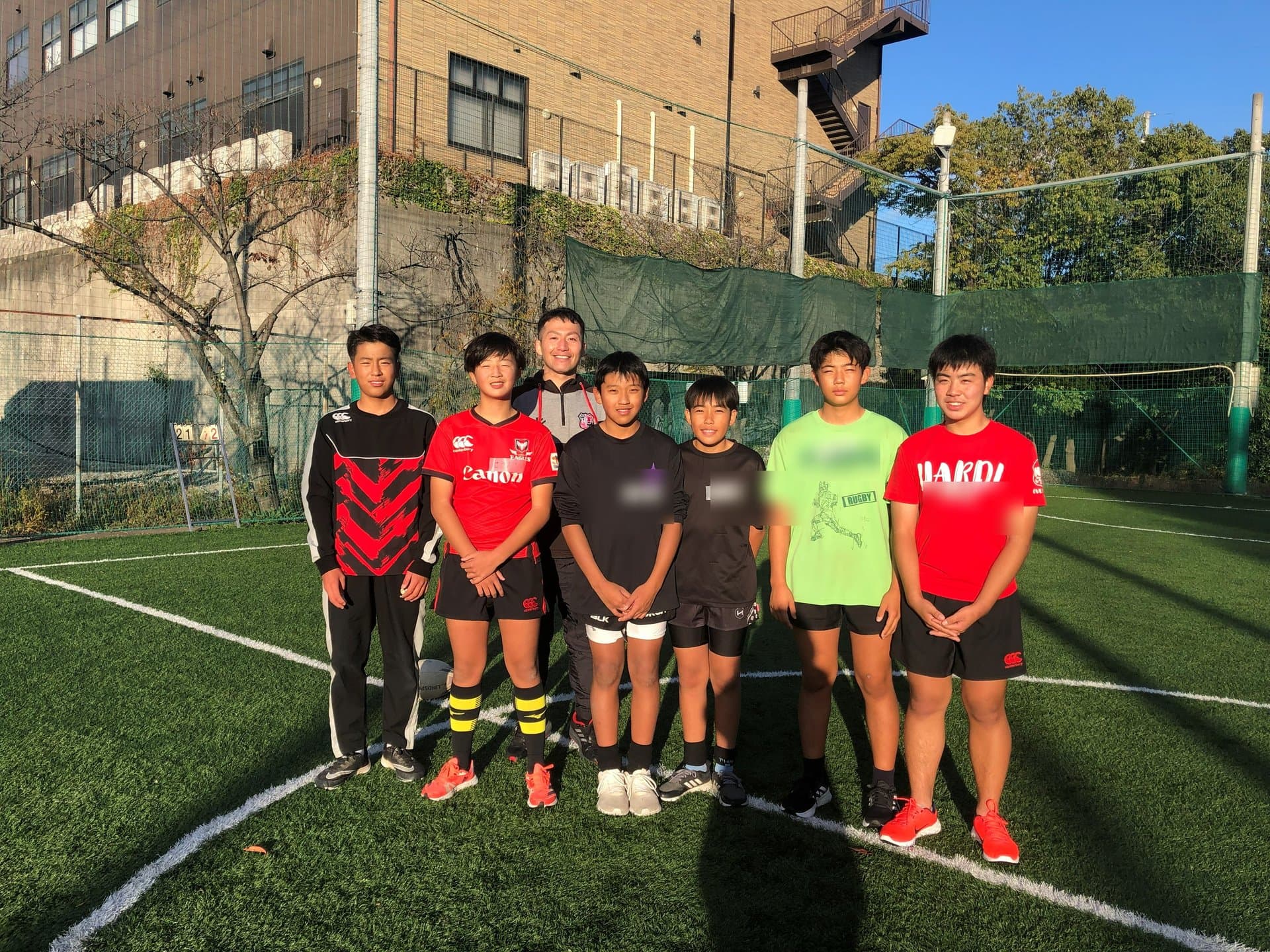 晴れたグラウンドに並ぶ小・中学生の選手たちとコーチ